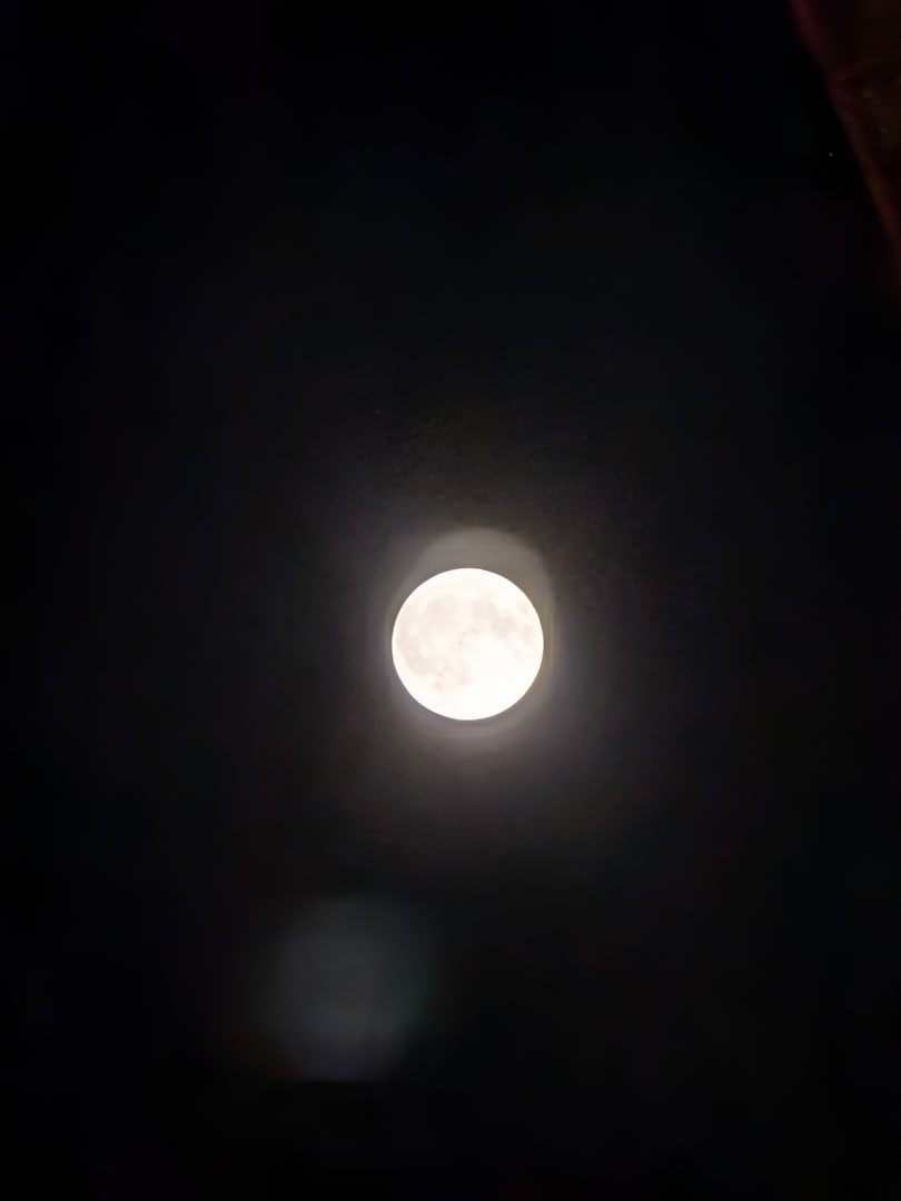 スマホ単体で撮影した満月。小さく写っており、周囲に薄雲による光のにじみが広がっている